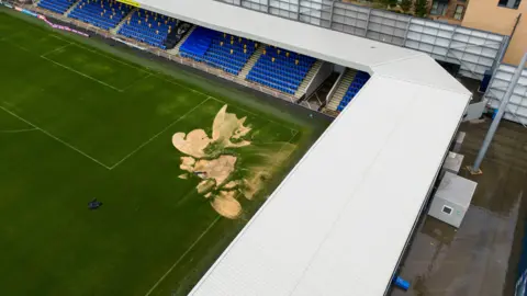 PA Media Aerial photo shows a sinkhole on the pitch and flooded walkways at the Cherry Red Records Stadium