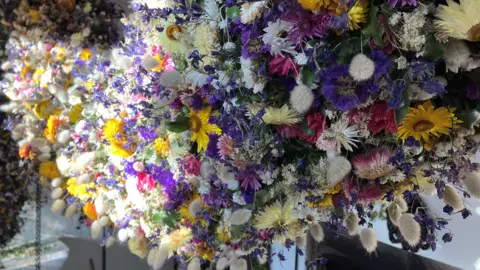 A close up of a myriad of flowers from bright yellow, white, cream, pink and purple adorn the garland