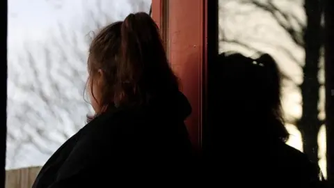 A woman poses in silhouette at her home. She was 14 when she was sexually abused by a grooming gang in Rochdale