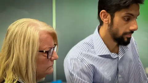 Jill Dalgleish and Dr Syed Junaid in a doctor's office. He is wearing a blue and white stripped button down shirt 