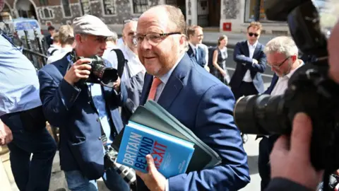 Getty Images George Freeman is holding a file and a book while surrounded by photographers.