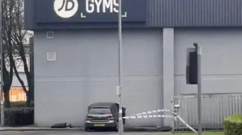 Dylan Winborne A silver or grey car has crashed into the wall of a JD Gym. There is a hole in the wall.