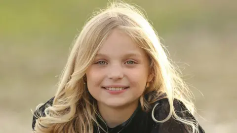 Portrait picture of Sophie smiling. The picture shows her with long blonde hair and wearing a dark top.