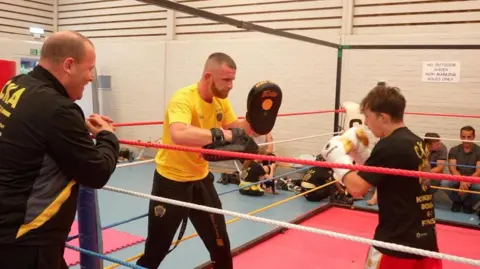 Jamie Niblock/BBC Leon Dunnett in the ring training a younger fighter while his father watches. 