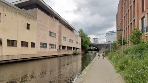 A streetview image of a towpath next to a canal, with a court building to the left of the canal