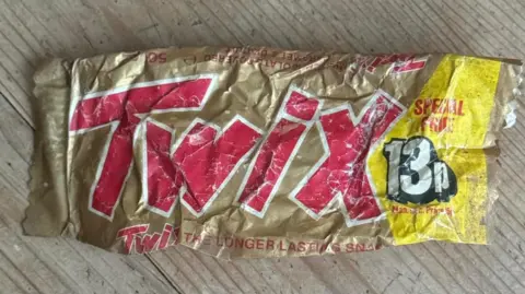 El Clarke A gold Twix wrapper. The word Twix is red and the on the right-hand side, it is yellow with the price of it which was 13p.