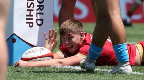 Steffan Emanuel lies on the line with the ball and celebrates scoring his second try for Wales Under-20s against Uruguay