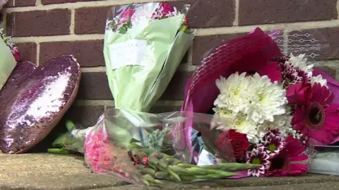 Floral tributes against a brick wall.