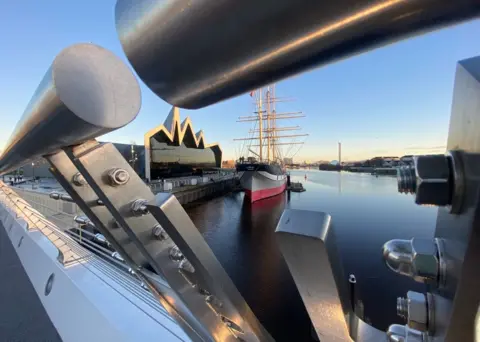 Christine Montgomery A view of Glasgow’s Riverside Museum and tall ship Glenlee on a sunny day, taken through the new Govan-Partick bridge. The River Clyde is still and there's a blue sky.
