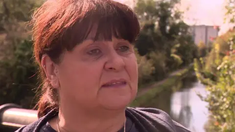 Wendy Hermon, a woman with dark hair tied back, standing on a canal bridge