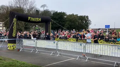 A view of the finish line with a few runners approaching a large crowd around