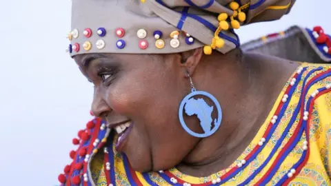 An image of a minister dressed up for Sona in traditional attire. A Africa shaped earring dangles 