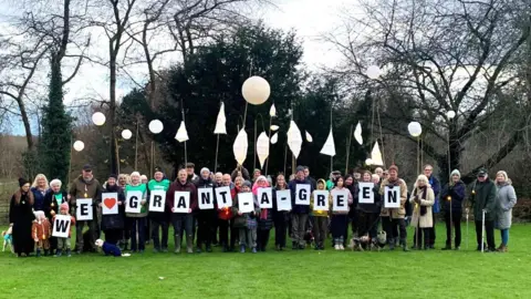 Blackwell Parkland campaigners with placards in December 2023. The placards read 'We love grant a green'. There are over 20 campaigners on the green with many holding up paper lanterns on sticks.