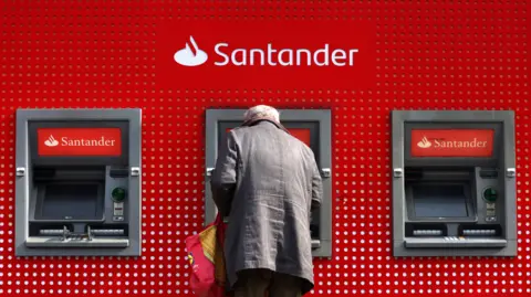 EPA-EFE/REX/Shutterstock Three ATM's with an elderly man standing with a bag operating the middle ATM. The Santander logo is above him and is visible on the two remaining ATM's.