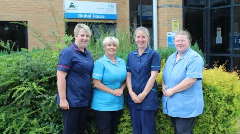 Four members of the community inclusion team standing alongside each other in a row outside a sand-coloured brick building in Scunthorpe. They are wearing blue and navy uniforms while smiling and looking directly at the camera.
