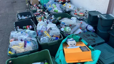 Overflowing boxes of recycling, along with food bins sitting out on a street