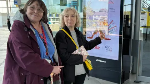 Marc Gaier/BBC Steff Hudson (right) has a black coat and trousers with a grey sweater. She has blonde hair and has a yellow handbag over her shoulder