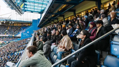 A photo of football fans and some of the Brown Girl Sport community watching Chelsea v Arsenal at Stamford Bridge in the Women's Super League 