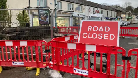 Red plastic barriers are blocking off the entrance to Newerne Street bridge in Lydney. A large sign reads Road Closed.