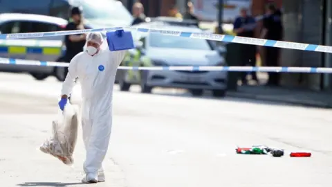 PA Media A forensics investigator at a crime scene walking under a length of police tape