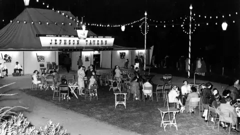 Maurice Mead Photography A black and white image showing people sat outside a marquee called Jephson Tavern. They are sat in groups around small tables.