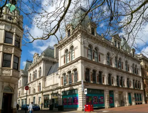 Getty Images A picture of Ipswich Corn Exchange, taken at street level. It is a grand-looking Victorian building fronted with light-coloured stone. Two cars are parked outside, and several people are walking past.