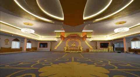 Guru Nanak Sikh Gurdwara A gold patterned carpet can be seen with the Sikh Khalsa sign added to the ceiling. There is a gold-looking platform at the back of the room and gold-decorated area for musicians.