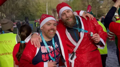 Two men with beards and Santa outfits and their Santa Dash medals