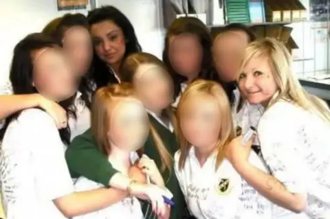 Family handout A photo of nine teenage girls posing for the camera, wearing either green school jumpers or white shirts. Handwritten notes in marker pen can be seen on the white shirts. All the girls’ faces are blurred, bar two.
