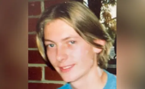 West Midlands Police Anthony Wilson, pictured as a younger man, wearing a blue t-shirt in front of a red-brick wall