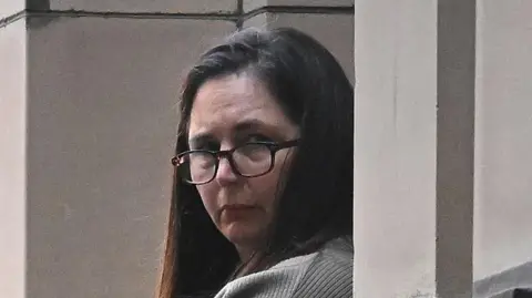 Erin Patterson, with long brown hair and wearing dark glasses, is looking over her left shoulder to the right