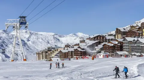 Image shows skiers amidst snow covered mountains at the Val Thorens ski resort.