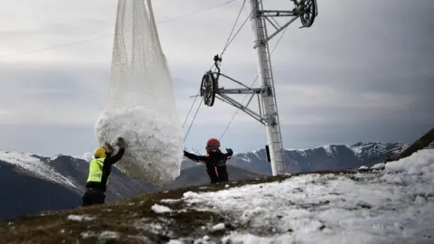 Getty Images Two men help a helicopter carrying snow near Luchon in French Pyrenees