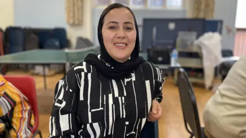 King's Arms Project Zarifa, a women sitting on a chair looking at the camera, wearing a black and white outside, and smiling