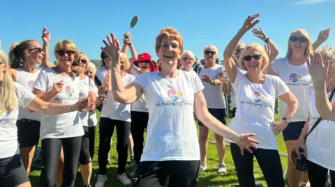 Doreen Manson is dancing in the middle of a group of older women wearing white t-shirts.