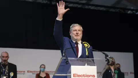 PA SNP candidate Angus Robertson stands on the stage with a hand waving, while the other candidates stand behind him