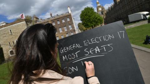 An employee from a betting company writes odds on a blackboard outside the Houses of Parliament in central London o