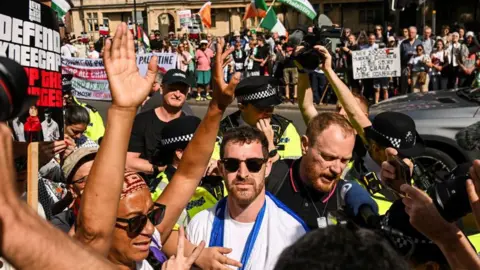 Reuters A crowd of people holding placards saying 'Defend Kneecap', and holding Palestinian flags outside the court in London