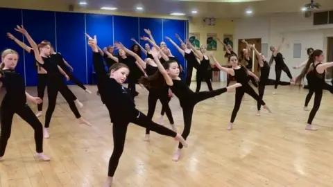 Children in a dance lesson and the are in the middle of doing a dance move. They are all wearing all black. 