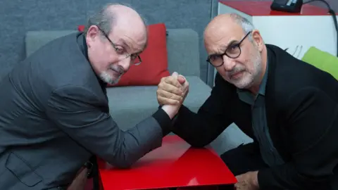 Salman Rushdie (left) and Alan Yentob arm wrestling while listening to opera in series one of W1A