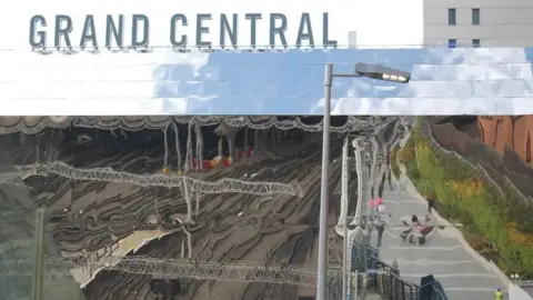 A photograph of the reflective panels on the Grand Central building, with a 'Grand Central' sign on top. 