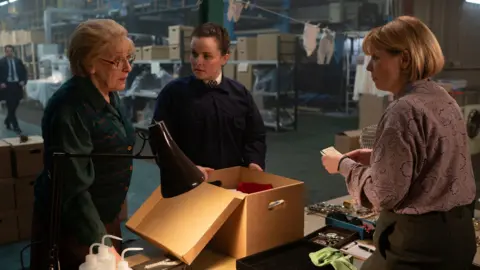 BBC/World Productions Two women and a female police officer from the drama in a warehouse full of the belongings of Lockerbie bomb victims