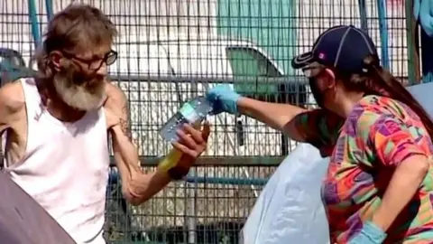 A community outreach worker hands water to a homeless person.