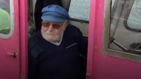 Ray Sedgwick sitting at the controls of the ferry, looking out from behind its pink sides
