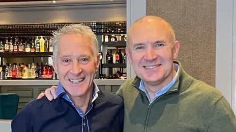 Rob Northfield A man with short white hair smiles standing next to a bald man. They are in a restaurant bar