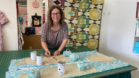 Julie Miles standing behind a measuring table cutting fabric