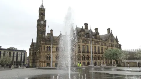 Neil Theasby/Geograph A large gothic town hall building with a tall clocktower. A fountain is in front of the building. A lower 1960s style building is to the left of the building.