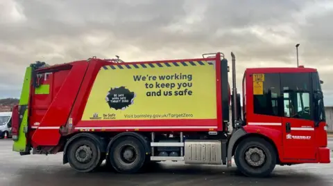 A red bin lorry with yellow stickers that read: We're working to keep you and us safe.