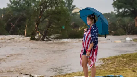 Woman stands with umbrella as river floods in background