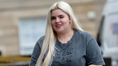 A blonde woman smiling while holding a handbag outside court 